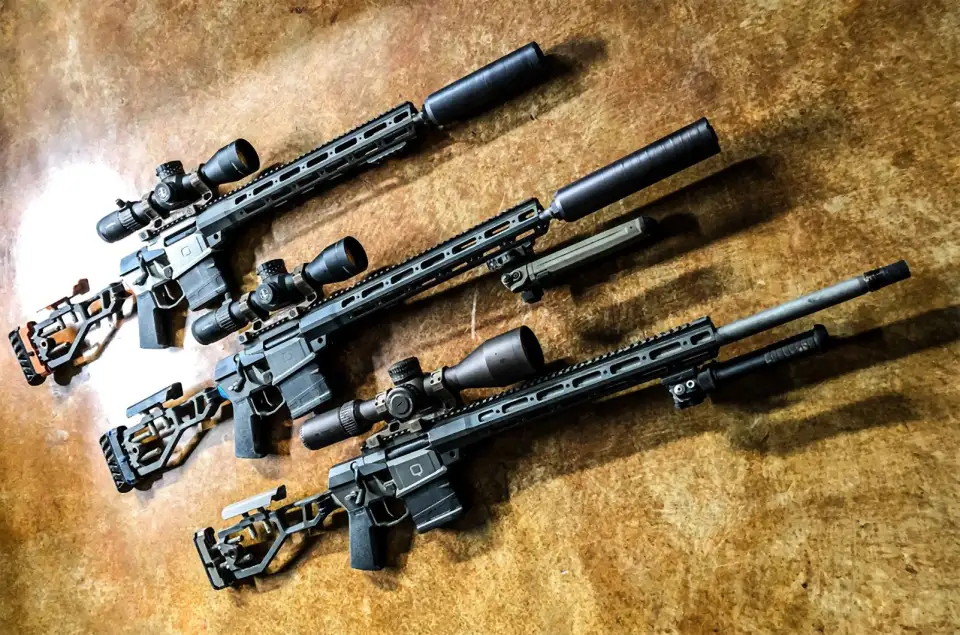 Three 3G Guns custom rifles with suppressors laid out on a wood table